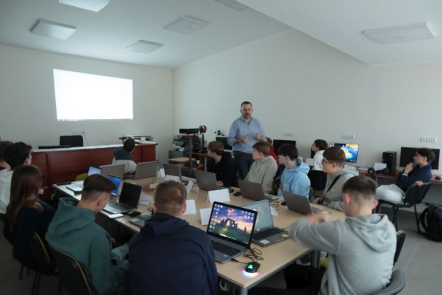 młodzież pracuje przy komputerach, obok nich stoi szkoleniowiec