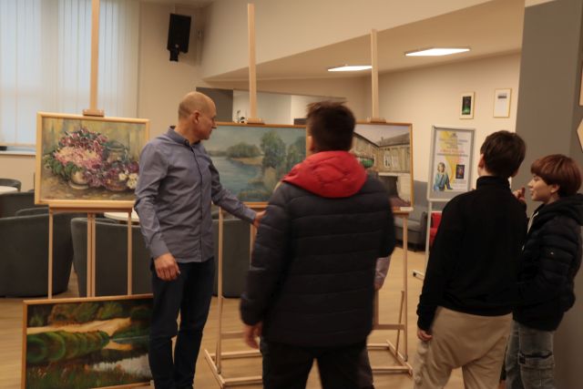 młodzież z nauczycielem oglądają wystawę obrazów w bibliotece