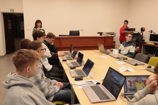 młodzież siedzi w sali komputerowej, przed nią stoi dyrektorka biblioteki oraz kobieta szkoląca