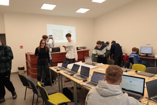 młodzież sczytuje kod QE ze ściany, część z nich siedzi przed laptopami