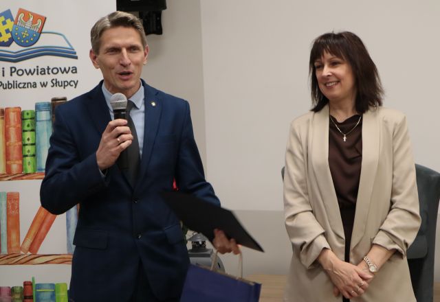 burmistrz z mikrofonem i granatową teczką, obok dyrektorka biblioteki