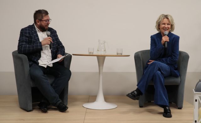 na scenie w fotelach siedzą prowadzący spotkanie z mikrofonem w dłoniach oraz Maria Pakulnis