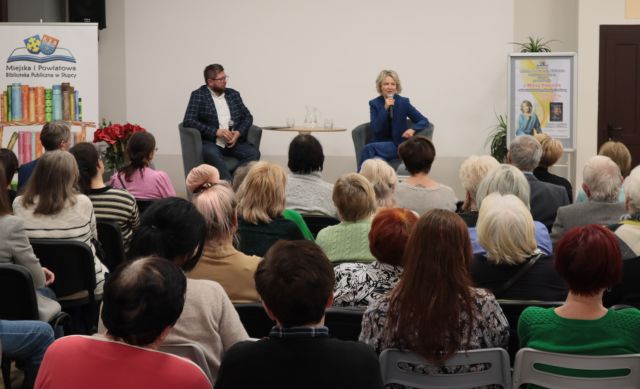 na zdjęciu uczestnicy spotkania siedzący na krzesłach, w tle siedzący na fotelach mężczyzna i kobieta