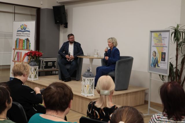 na zdjęciu uczestnicy spotkania siedzący na krzesłach, w tle siedzący na fotelach mężczyzna i kobieta