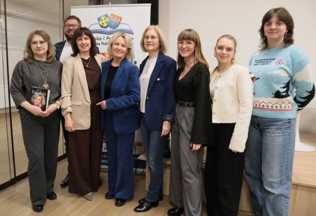 5 bibliotekarek, dyrektorka biblioteki i prowadzący spotkanie pozują do zdjęcia z aktorką Marią Pakulnis