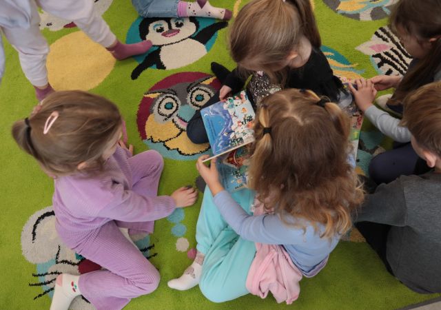 dzieci na kolorowym dywanie przeglądają książk