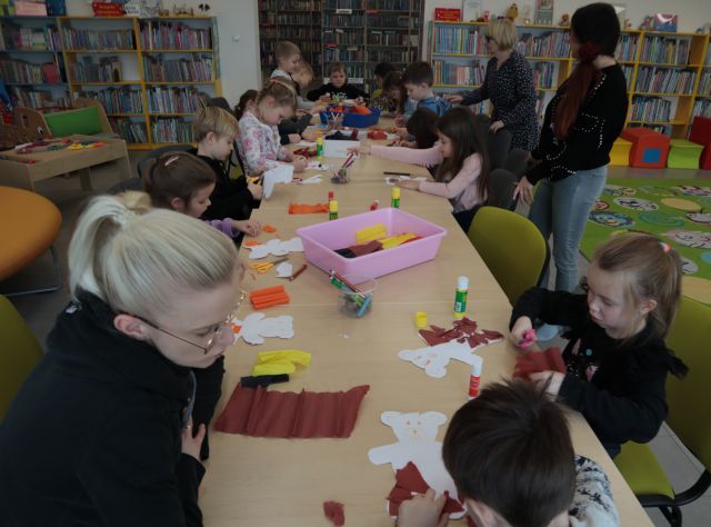 dzieci soedzą przy stołach i malują na kartkach i wycinają misie