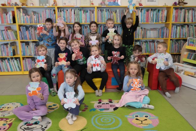 przedszkolaki ze swoimi misiami z kartek pozują do grupowego zdjęcia, w tle regały z książkami