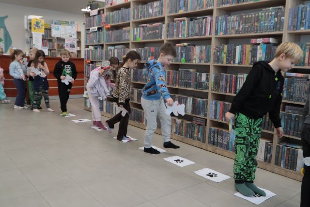 dzieci idą po kartkach, w tle regały z książkami