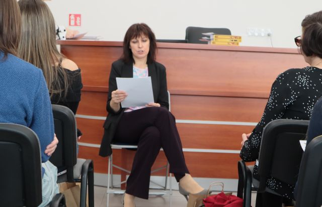 dyrektorka biblioteki siedzi na krześle i czyta z kartki, przed nią na krzesłąch siedzą uczestnicy konkursu