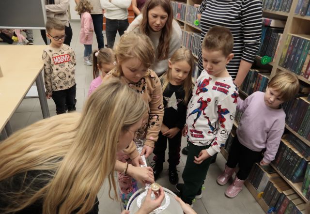 bibliotekarka odczytuje z kartki andrzejkową wróżbę stojącym wokół dzieciom