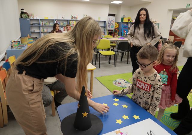 bibliotekarka przykleja gwiazdy na niebieski papier, przed nią stoją dzieci
