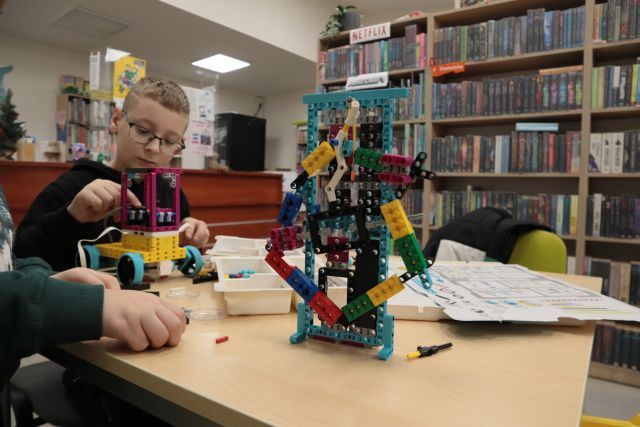 chłopcu budują z klockó Lego, przed nimi maszyna i budowla z klocków