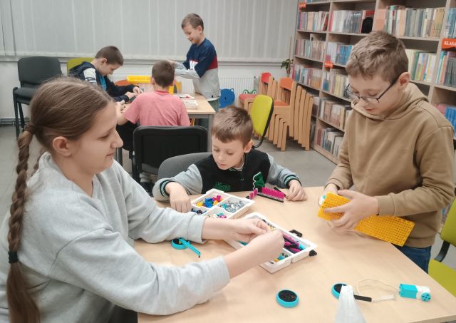 dzieci przy stolikach składają klocki Lego