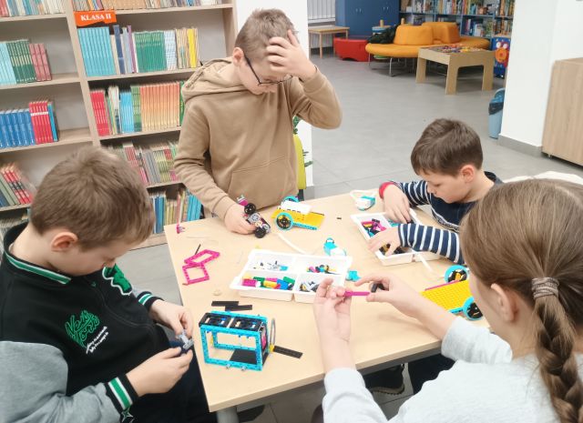 3 chłopcó i dziewczynka budują z klocków Lego