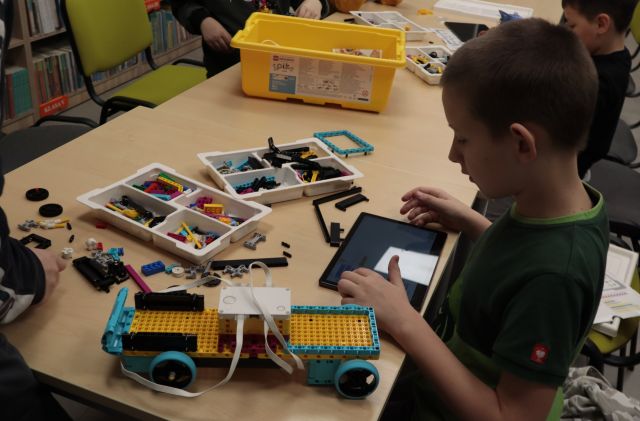 chłopiec z labletem, na stole klocki Lego