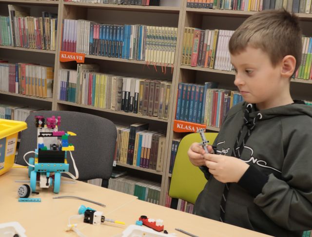 chłopiec, przed nim na stole pojazd z klocków Lego, w tle regały z książkami