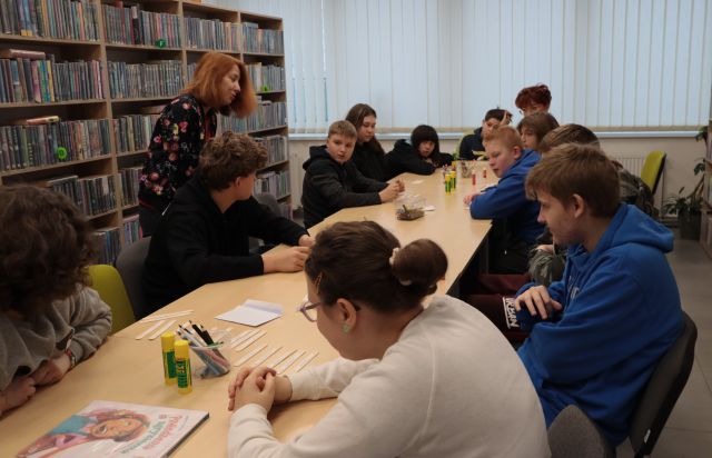 młodzież siedzi przy stole i układa przysłowia naklejone na patyczki