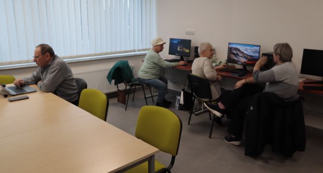 3 seniorki i 1 senior pracują przy komputerach i laptopie