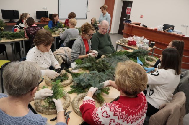 uczestnicy warsztatów przy stołąch robią wianki świąteczne