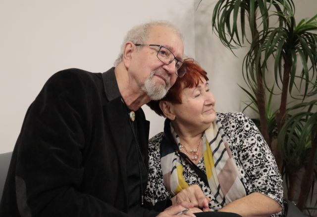Na zdjęciu widać od pasa w górę mężczyznę oraz kobietę, stykają się głowami. Za nimi znajduję się zielona roślina.