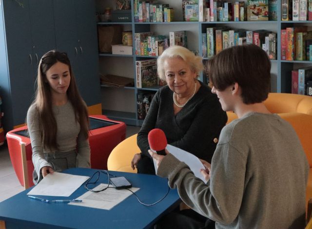 chłopak mówi do mikrofonu, przed nim siedzi kobieta i dziewczyna