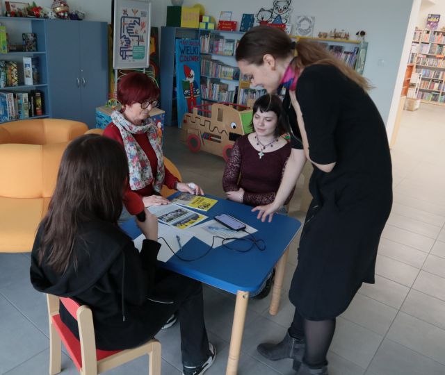 dziewnnikarka stoi nad dwiema dziewczynami i kobietą siedzącymi przy stole