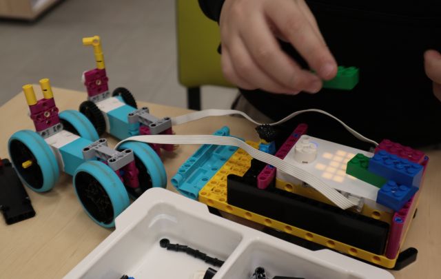 Na zdjęciu widać sanie ciągnięte przez renifery wykonane z klocków Lego. a zdjęciu znajduję się również ręka chłopca z klockiem.