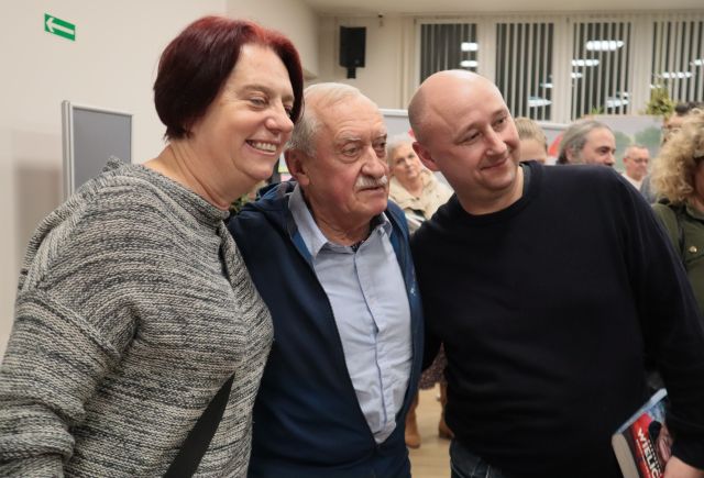 Na zdjęciu znajduję się Krzysztof Wielicki, po jego prawej stronie stoi kobieta, a po lewej mężczyzna. W tle znajdują się okna.
