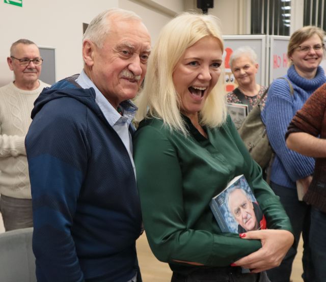 Na zdjęciu znajduję się Krzysztof Wielicki oraz uśmiechnięta kobieta stojąca po prawej stronie z książką. W tle znajdują się ludzie.