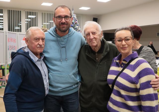 Na zdjęciu znajduję trójka mężczyzn oraz jedna kobieta, wszyscy pozują do wspólnego zdjęcia. W tle znajdują się okna oraz choinka.