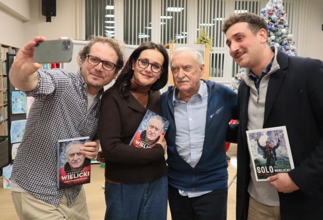 Na zdjęciu znajduję się kobieta oraz trzech mężczyzn w tym Krzysztof Wielicki, mężczyzna po lewej stronie ma wyciągniętą rękę z telefonem i robi im wspólne zdjęcie, trójka osób trzyma w ręce książkę.