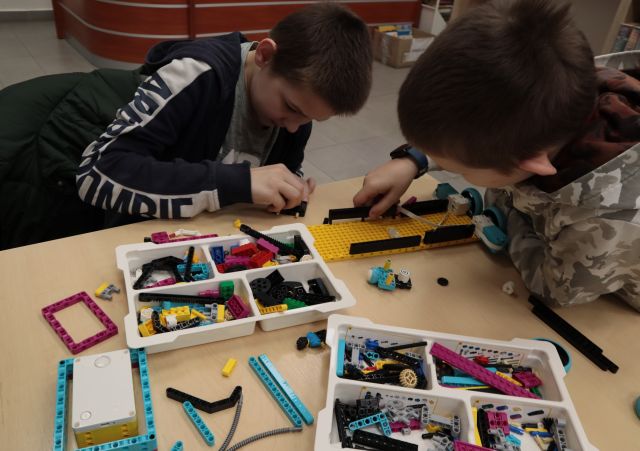 Na zdjęciu znajduję się dwójka chłopców składających LEGO przy stoliku.