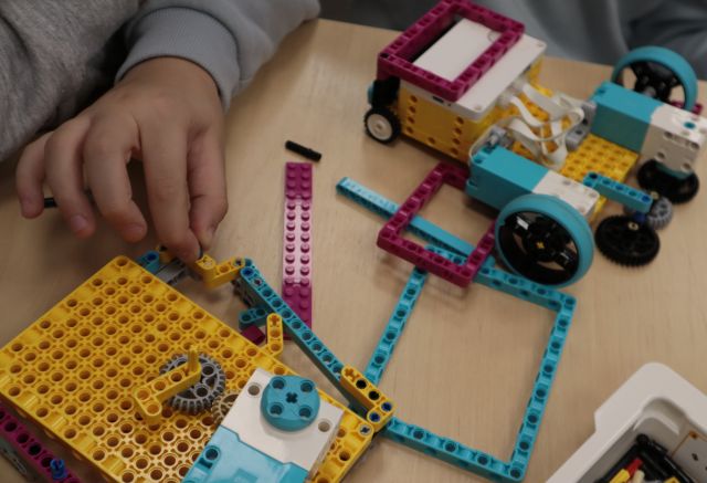 Na zdjęciu znajdują się roboty z Lego w trakcie składania oraz ręka chłopca.