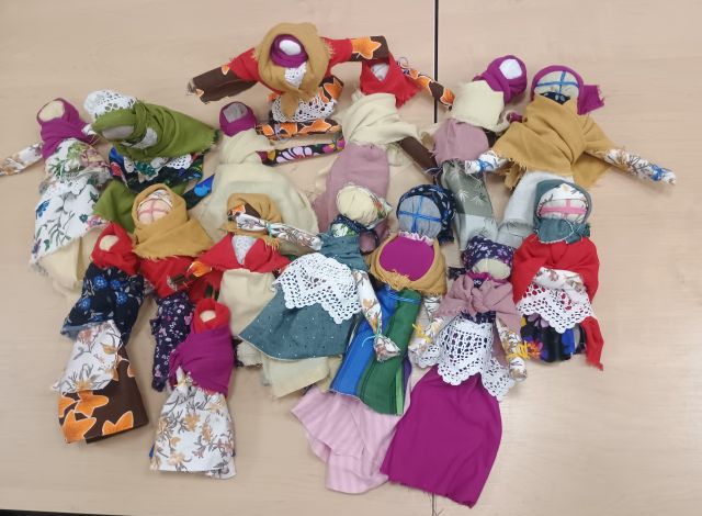 Na zdjęciu znajduje się piętnaście wykonanych na zajęciach motanych lalek leżących na stole.