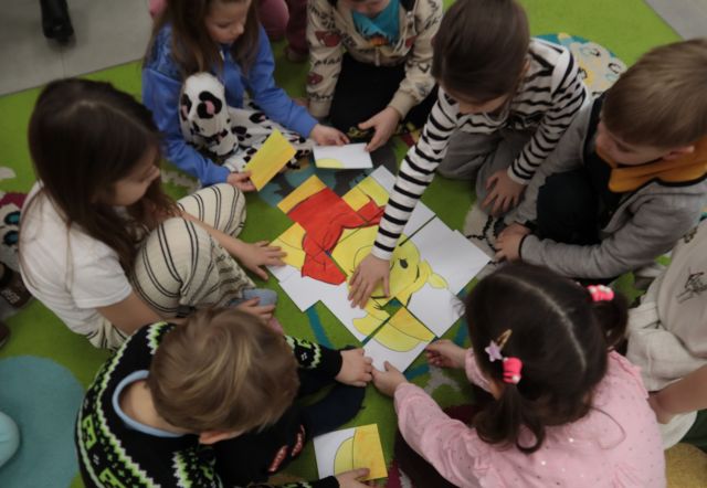 Na zdjęciu znajdują się przedszkolaki, które układają puzzle z Kubusia Puchatka na dywanie.