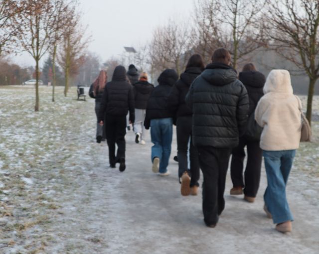 Na zdjęciu znajduje się idąca młodzież przez park zimą.