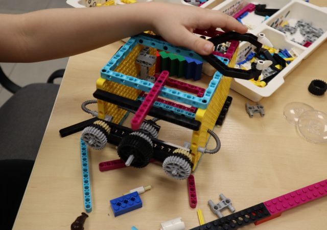 Na zdjęciu znadjuje się zbudowana rakieta z LEGO Education, trzymana przez rękę chłopca, dookoła leżą klocki LEGO.