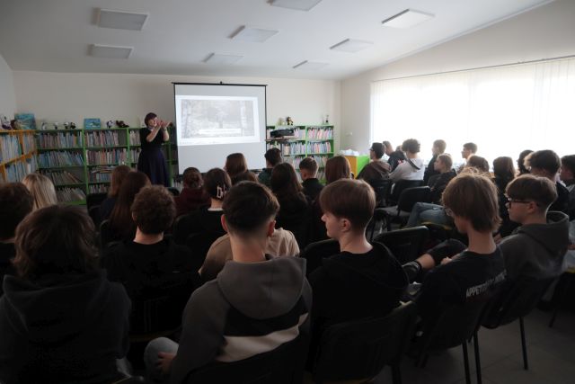 Na zdjęciu znajduje się młodzież z Liceum siedząca na wprost kobiety przedstawiającej prezentacje o Słowianach. W tle za kobietą znajdują się półki z książkami.
