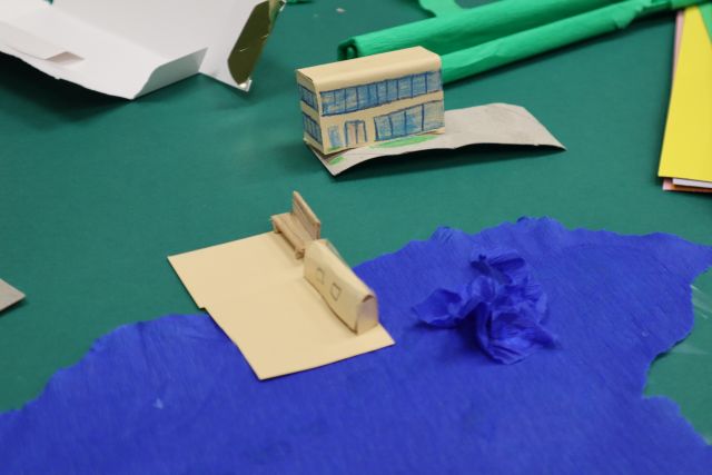 Na zdjęciu znajduje się fragment makiety przedstawiający budynki nad wodą oraz szkołę w oddali na zielonym brystolu.