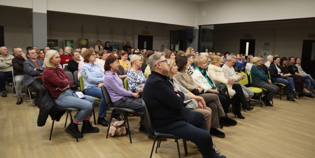 Na zdjęciu znajduje się około 110 osób, widowni, którzy są skierowani w stronę sceny. Zdjęcie zostało wykonane od boku.