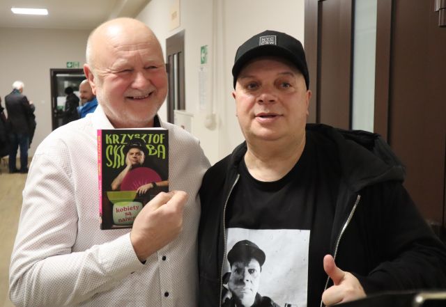 Na zdjęciu znajduje się dwóch mężczyzn pozujących do zdjęcia, jeden trzyma w ręce książkę.