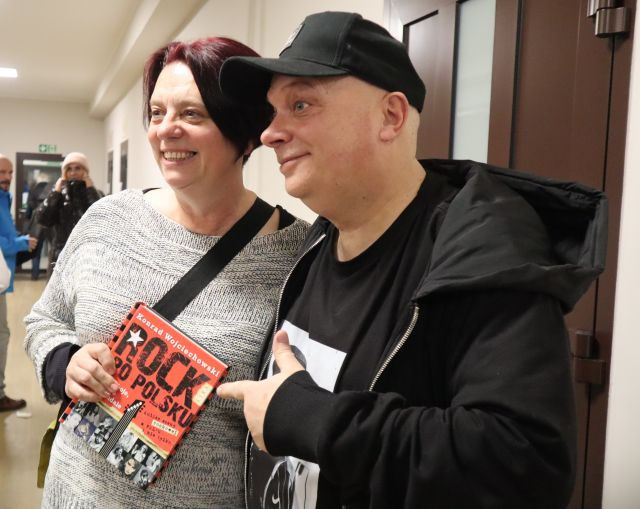 Na zdjęciu znajduje się Krzysztof Skiba wraz z kobietą, która trzyma książkę Rock po polsku. Zdjęcie zostało wykonane od boku.