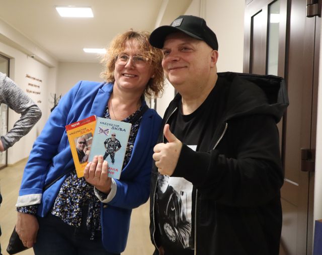 Na zdjęciu znajduje się kobieta pozująca do zdjęcia Krzysztofem Skibą, kobieta trzyma w ręce dwie książki.