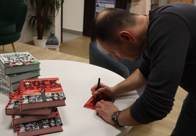 Na zdjęciu znajduje się Konrad Wojciechowski nachylony nad stolikiem i podpisujący płytę, obok leżą książki Rock po Polsku oraz Perfect bo idole po to żyją