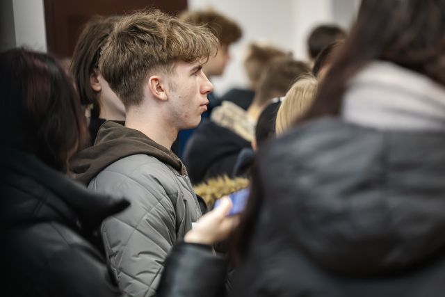 Na zdjęciu w centrum znajduje się twarz chłopaka bokiem, a dookoła niego znajdują się inni uczniowie.