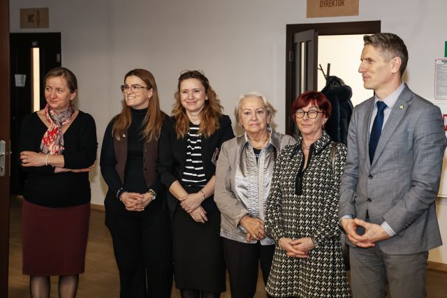Na zdjęciu znajduje się pięć stojących kobiet oraz jeden mężczyzna, za nimi w tle są otwarte drzwi.