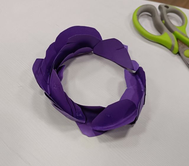 Na zdjęciu znajduje się kwiat z fioletowych kartek, kwiat znajduje się na stole, a obok leżą nożyczki.