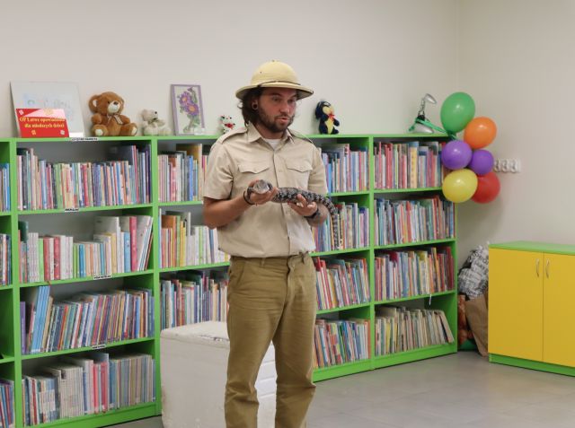 mężczyzna podróżnik z jaszczurką, w tle regały z książkami