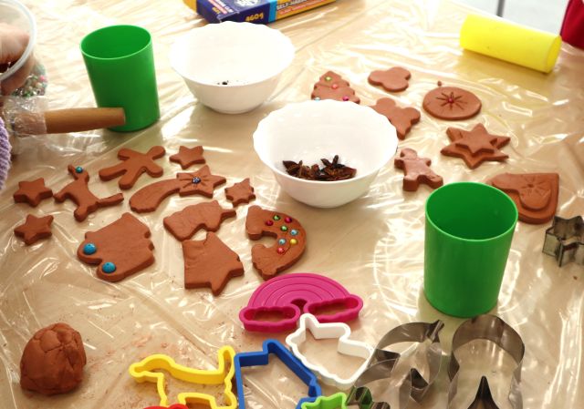 Na zdjęciu znajduje się stół z piernikami z gliny, część z nich jest ozdobiona, na stolikach leżą również kubki i miseczki z ozdobami.